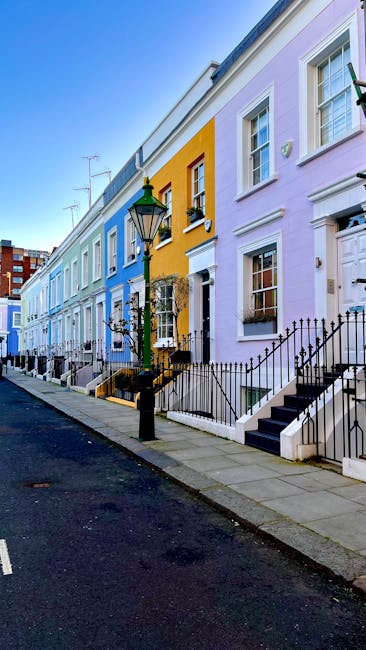 Image showing a row of Victorian-style terraced houses with decorative bay windows and painted facades in various colors, including light blue, teal, beige, black, and bright green, under natural daylight. The buildings feature brick and stucco exteriors with detailed cornices and window frames. A black streetlamp is visible in the foreground, standing on a sidewalk with a parking sign nearby. The scene depicts a clean, residential street in Islington, with well-maintained facades and no visible dirt or wear, representing a tidy urban environment. This setting exemplifies the type of properties that [COMPANY_NAME] provides professional cleaning services for, including end of tenancy cleaning and surface cleaning in the Upper Street Angel area of Islington.