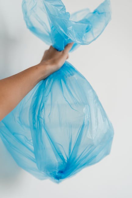 A large blue recycling bin with a closed lid positioned next to the rear wheel of a white mobile food truck or catering van, which has a plain metal surface showing some dirt and minor scrapes. The bi